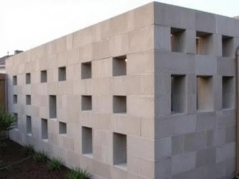 
A modern geometric cinder block privacy screen wall with alternating solid and open sections creating an artistic pattern, minimalist backyard setting, clean lines and contemporary design, shot from an angle showing depth and dimension, soft evening lighting